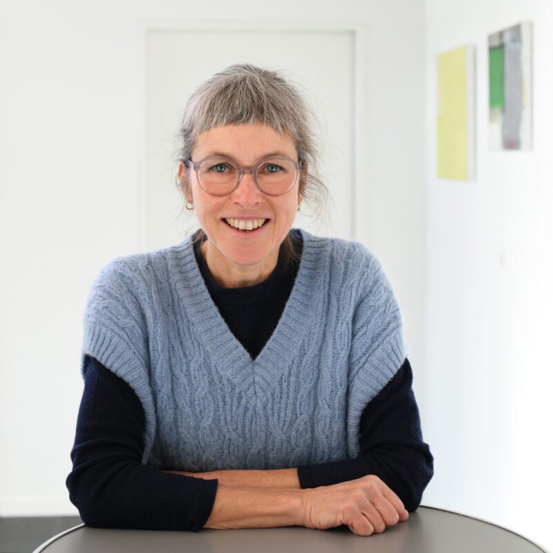 Silvia Bolliger steht an einem Tisch und lächelt in die Kamera.