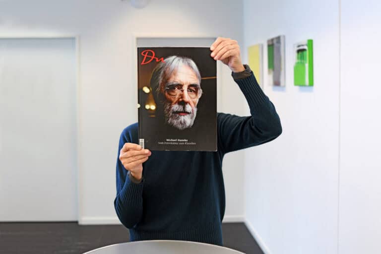 Angelika Gleichmann hält sich ein DU Magazin so vor den Kopf, dass der Kopf vom Titelbild, von Michael Haneke den Ihren ersetzt.