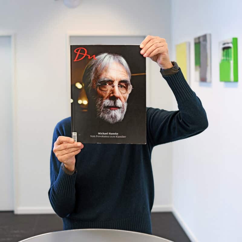 Angelika Gleichmann hält sich ein DU Magazin so vor den Kopf, dass der Kopf vom Titelbild, von Michael Haneke den Ihren ersetzt.