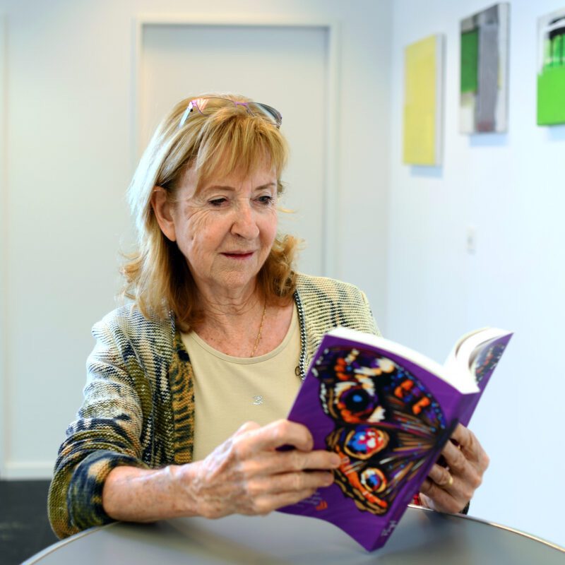 Elisabeth Spreng Troller hält ein violettes Buch mit einem Seitenfüllenden Schmetterlingsflügel in der Hand, welches sie selbst geschrieben hat.