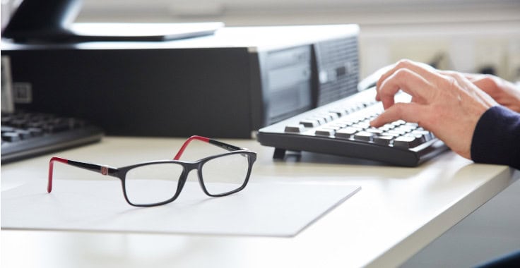 Content Bild, auf welchem eine Person auf einer Computer Tastatur tippt. Eine Brille liegt auf einem Blatt Papier neben der Tastatur.